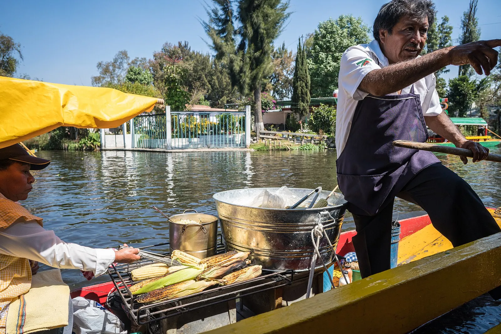 En bådfører, der står agter i en lille båd på en kanal i Xochimilco og griller majs på en kulgrill