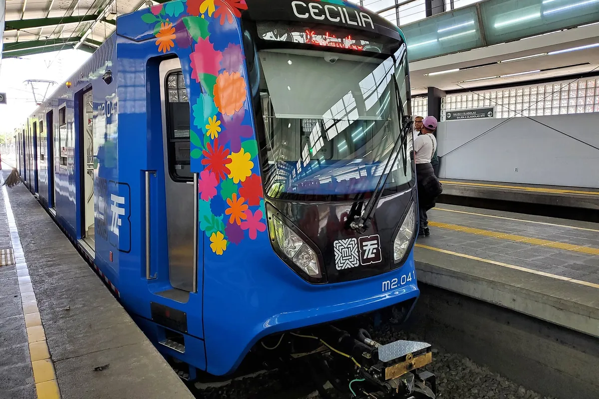 Modrobílý vlak lehké železnice vyzdobený květinami stojící u nástupiště stanice Xochimilco