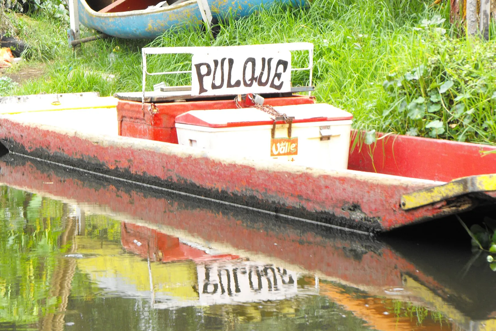 En rød båd på en kanal i Xochimilco med en køleboks og et håndmalet skilt, hvor der står pulque